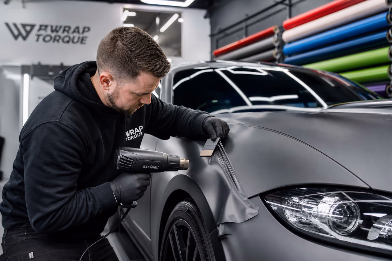 Technician Applying Vinyl Wrap to Luxury Car in Studio