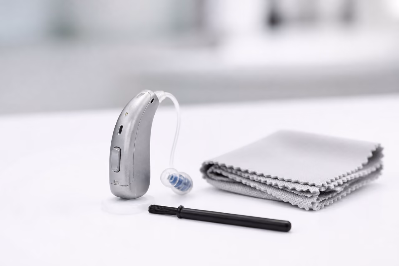 Modern Hearing Aid and Cleaning Kit on White Surface